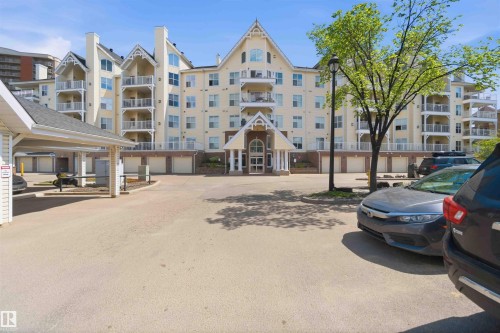 Multi-story building with multiple balconies, covered parking structure, ground-level garage access, and prominent entrance portico - #104 10221 111 St Nw, Edmonton, AB - Outdoor With Facade