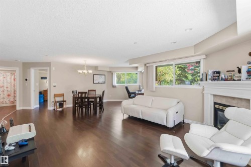 Expansive wood-finish flooring throughout, recessed ceiling lighting, a built-in fireplace with a mantel, and multiple windows providing natural light - #104 10221 111 St Nw, Edmonton, AB - Indoor Photo Showing Living Room With Fireplace