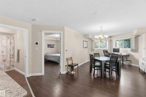 Open-concept living area featuring rich wood-finish flooring, a multi-light chandelier, and large windows with natural light - #104 10221 111 St Nw, Edmonton, AB - Indoor Photo Showing Dining Room