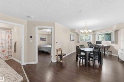 Open-concept living area featuring rich wood-finish flooring, a multi-light chandelier, and large windows with natural light - 