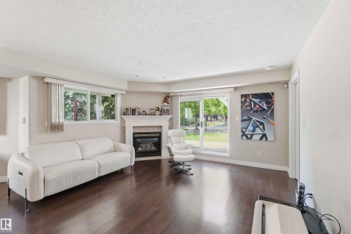 Living area with wood-finish flooring, a built-in fireplace, multiple windows with blinds, and a sliding glass door - #104 10221 111 St Nw, Edmonton, AB - Indoor Photo Showing Living Room With Fireplace