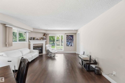 Spacious living area featuring dark wood-finish flooring, a white mantel fireplace, and sliding glass doors to the exterior - #104 10221 111 St Nw, Edmonton, AB - Indoor Photo Showing Living Room With Fireplace
