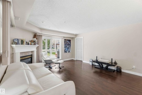 Fireplace with an ornate white mantel, wood-finish flooring, recessed lighting, sliding glass door, and neutral wall tones - #104 10221 111 St Nw, Edmonton, AB - Indoor Photo Showing Living Room With Fireplace