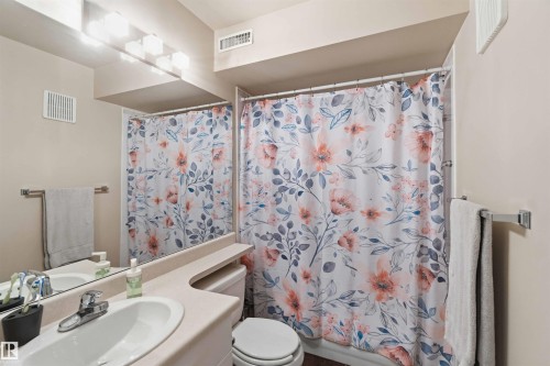 Bathroom featuring a vanity with an integrated sink, polished chrome faucet, and a large mirror - #104 10221 111 St Nw, Edmonton, AB - Indoor Photo Showing Bathroom
