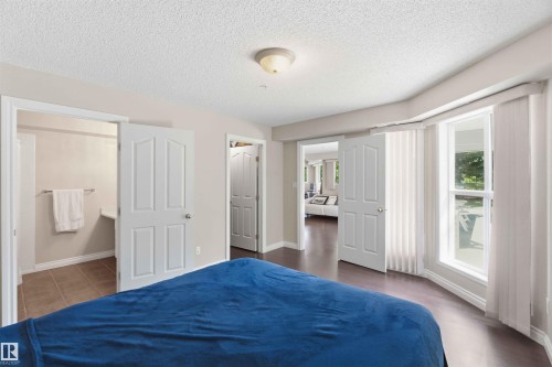 Dual panel doors, wood-finish flooring, and multiple windows with vertical blinds - #104 10221 111 St Nw, Edmonton, AB - Indoor Photo Showing Bedroom