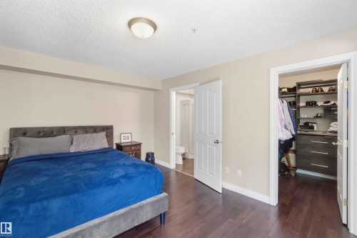 Spacious bedroom with dark wood-finish flooring, light neutral-toned walls, and a built-in closet organization system featuring shelving and drawers - #104 10221 111 St Nw, Edmonton, AB - Indoor Photo Showing Bedroom