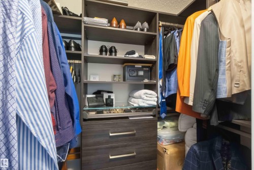 Built-in custom closet system featuring integrated shelving, multiple hanging rods, and wood-finish drawers with modern hardware - #104 10221 111 St Nw, Edmonton, AB - Indoor With Storage