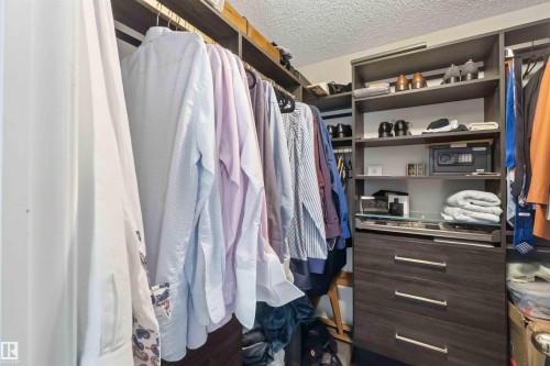 Built-in closet system featuring multiple hanging rods, open shelving, integrated drawers with horizontal hardware, and a glass-topped display shelf - #104 10221 111 St Nw, Edmonton, AB - Indoor With Storage
