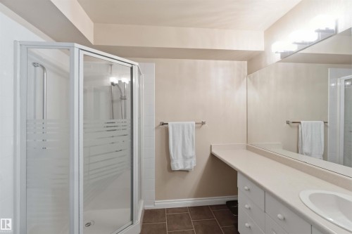 Corner shower enclosure with frosted glass panels, an integrated vanity with a white countertop, an undermount sink, and extensive mirrored wall coverage - #104 10221 111 St Nw, Edmonton, AB - Indoor Photo Showing Bathroom