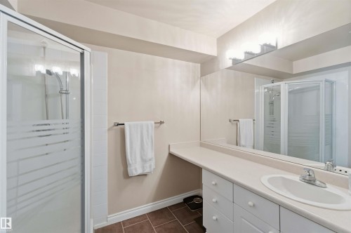 White vanity with integrated sink, expansive mirror, three-light vanity bar, glass-enclosed shower, and tiled flooring - #104 10221 111 St Nw, Edmonton, AB - Indoor Photo Showing Bathroom