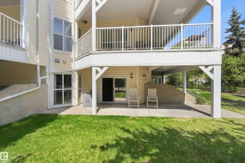 Ground-level patio with direct lawn access, featuring a sliding glass door entry and an overhead balcony - #104 10221 111 St Nw, Edmonton, AB - Outdoor With Exterior