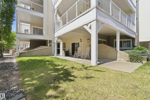 Ground-level patio with sliding glass door entry, concrete flooring, and surrounding green space - #104 10221 111 St Nw, Edmonton, AB - Outdoor
