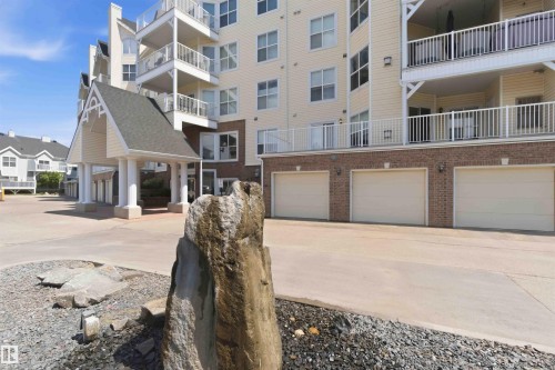 Multi-story building featuring a covered portico entry, multiple balconies with white railings, a brick facade base, and integrated garage doors - #104 10221 111 St Nw, Edmonton, AB - Outdoor With Facade