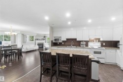 Open-concept kitchen and dining area featuring white cabinetry with quartz countertops, stainless steel appliances, a large center island with seating for three, wood-finish flooring throughout, and recessed lighting - 