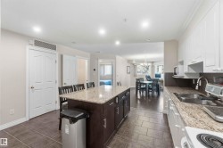 Kitchen featuring a large island with stone countertop, dark wood-finish cabinetry, white upper and lower cabinetry, and tile flooring - 