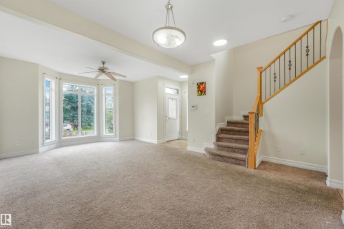 Bay window with multiple panes, ceiling fan, and staircase with wood handrail and wrought iron balusters - 10234 155 Street Nw, Edmonton, AB - Indoor Photo Showing Other Room