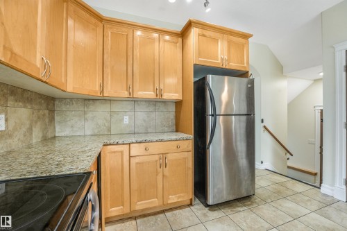 Kitchen featuring wood cabinetry, stone countertops, stainless steel refrigerator, tile backsplash, and tile flooring - 10234 155 Street Nw, Edmonton, AB - Indoor Photo Showing Kitchen
