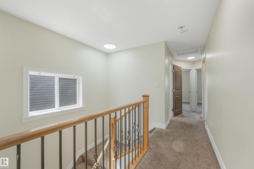 Carpeted upper-level hallway with a wood and wrought iron staircase railing, white window trim, and recessed ceiling lighting - 10234 155 Street Nw, Edmonton, AB - Indoor Photo Showing Other Room