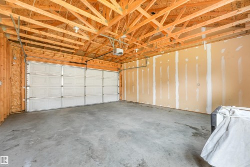 Unfinished garage space featuring a concrete floor, exposed wood ceiling trusses, a paneled garage door, and a garage door opener system - 10234 155 Street Nw, Edmonton, AB - Indoor Photo Showing Garage