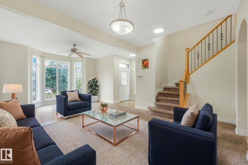 Bay window with multiple panes, ceiling fan, carpeted staircase with wood handrail and wrought iron balusters, recessed lighting, and a front entry door with glass panels - 10234 155 Street Nw, Edmonton, AB - Indoor Photo Showing Living Room