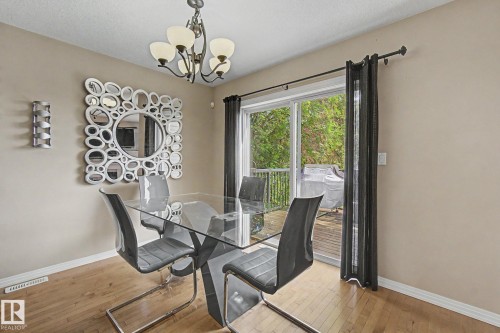 Hardwood-style flooring, sliding glass door with exterior deck access, and an overhead chandelier with frosted glass shades - 9935 155 Street Nw, Edmonton, AB - Indoor Photo Showing Dining Room