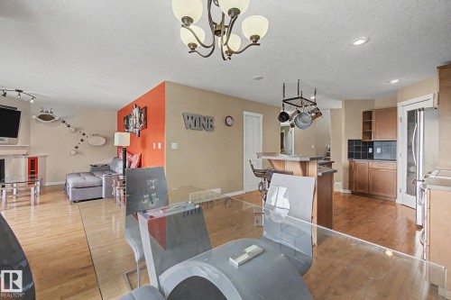 Open concept living area featuring wood-finish flooring, a kitchen with wood cabinetry and black tile backsplash, and a dining area with a glass-top table - 9935 155 Street Nw, Edmonton, AB - Indoor Photo Showing Other Room