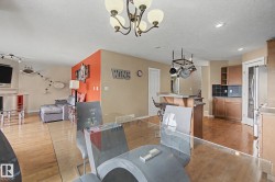 Open concept living area featuring wood-finish flooring, a kitchen with wood cabinetry and black tile backsplash, and a dining area with a glass-top table - 
