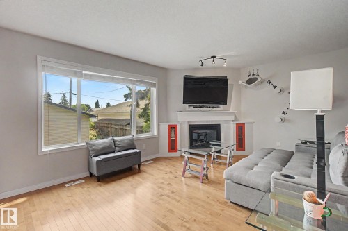 Hardwood flooring throughout, a large window providing abundant natural light, a built-in fireplace with a mantel, and recessed shelving with accent details - 9935 155 Street Nw, Edmonton, AB - Indoor Photo Showing Living Room With Fireplace
