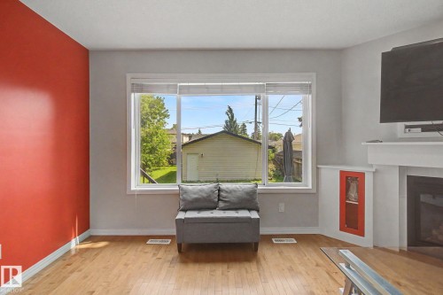 Wood-finish flooring, white trim, red accent wall, white-framed window, and built-in fireplace - 9935 155 Street Nw, Edmonton, AB - Indoor Photo Showing Living Room With Fireplace