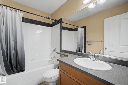 White tub and shower combination with dark tile surround, single vanity with integrated sink, and polished chrome faucet - 9935 155 Street Nw, Edmonton, AB - Indoor Photo Showing Bathroom