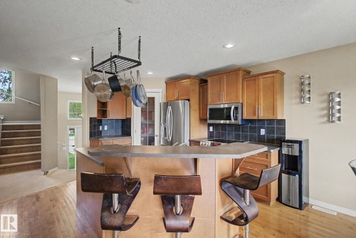 Hardwood-finish flooring, recessed lighting, wood cabinetry, dark tile backsplash, and stainless steel appliances - 9935 155 Street Nw, Edmonton, AB - Indoor Photo Showing Kitchen