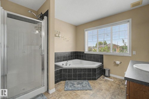 Walk-in shower enclosure, corner soaking tub with dark tile surround, and a vanity with a white sink and dark countertop - 9935 155 Street Nw, Edmonton, AB - Indoor Photo Showing Bathroom