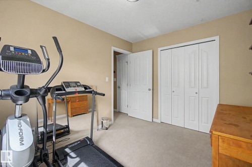 Light beige wall paint, white trim, light gray carpet, white bi-fold closet doors, and a white interior door - 9935 155 Street Nw, Edmonton, AB - Indoor Photo Showing Gym Room