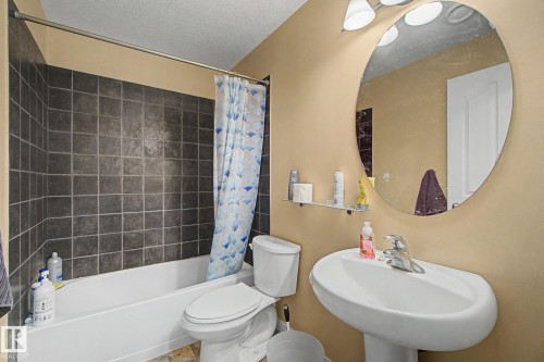 Full bath with dark-toned wall tiles, a white porcelain tub, a pedestal sink, and a large oval mirror - 9935 155 Street Nw, Edmonton, AB - Indoor Photo Showing Bathroom