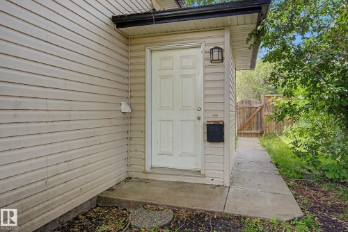 Light-colored siding exterior with a paneled entry door and exterior wall sconce - 9935 155 Street Nw, Edmonton, AB - Outdoor With Exterior