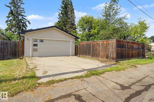 Detached garage with siding exterior, sectional overhead door with windows, concrete driveway, and surrounding wood fencing - 9935 155 Street Nw, Edmonton, AB - Outdoor