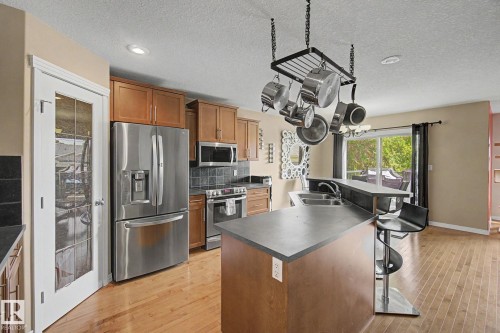 Kitchen featuring stainless steel appliances, wood-finish flooring, a two-tiered kitchen island with a built-in sink, and a sliding glass door - 9935 155 Street Nw, Edmonton, AB - Indoor Photo Showing Kitchen With Double Sink