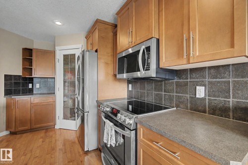 Wood-finish flooring, light wood cabinetry, dark tile backsplash, stainless steel appliances, and solid surface countertops - 9935 155 Street Nw, Edmonton, AB - Indoor Photo Showing Kitchen