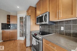 Wood-finish flooring, light wood cabinetry, dark tile backsplash, stainless steel appliances, and solid surface countertops - 