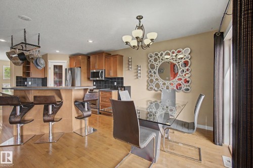 Kitchen island with bar seating, wood-finish flooring, stainless steel appliances, and a tile backsplash - 9935 155 Street Nw, Edmonton, AB - Indoor Photo Showing Dining Room