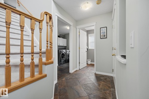 Wood banister with turned spindles, carpeted staircase, stone-finish tile flooring, built-in cabinetry, and ceiling-mounted light fixture - 15 Orchid Place, St. Albert, AB - Indoor Photo Showing Other Room