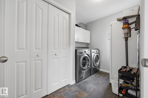 Laundry area featuring stainless steel front-load machines, white cabinetry, dark stone-finish flooring, and bifold doors - 15 Orchid Place, St. Albert, AB - Indoor Photo Showing Laundry Room