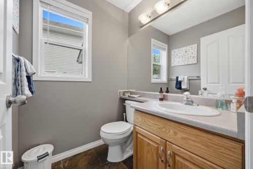 Bathroom featuring a single window, a built-in wood-finish vanity with an integrated sink, a vanity light fixture, and dark-toned flooring - 15 Orchid Place, St. Albert, AB - Indoor Photo Showing Bathroom