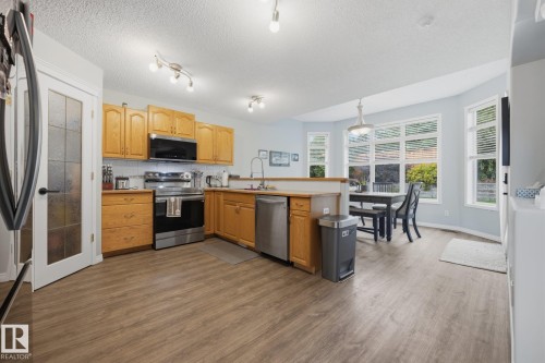 Wood-finish flooring throughout, wood cabinetry, stainless steel appliances, and a dining area with multiple windows - 15 Orchid Place, St. Albert, AB - Indoor Photo Showing Kitchen