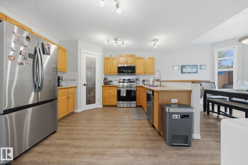 Wood-finish flooring, stainless steel appliances, light wood cabinetry, white tile backsplash, and a glass-paneled interior door - 15 Orchid Place, St. Albert, AB - Indoor Photo Showing Kitchen