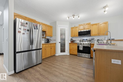 Wood-finish flooring, stainless steel appliances, light wood cabinetry, track lighting, and a frosted glass pantry door - 15 Orchid Place, St. Albert, AB - Indoor Photo Showing Kitchen