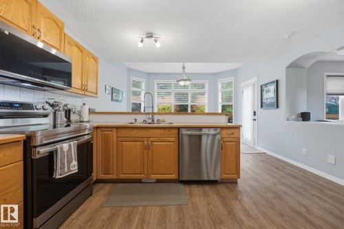 Wood-finish flooring throughout, stainless steel appliances, light wood cabinetry, white subway tile backsplash, and a large bay window - 15 Orchid Place, St. Albert, AB - Indoor Photo Showing Kitchen