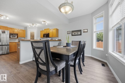 Vaulted ceiling with an ornamental chandelier, multiple windows, wood-finish flooring, and light wood cabinetry with stainless steel appliances - 15 Orchid Place, St. Albert, AB - Indoor Photo Showing Dining Room