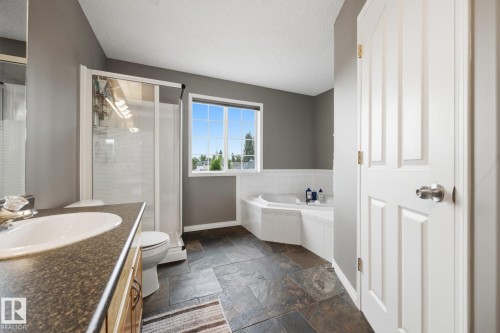 Spacious bathroom featuring a built-in bathtub with white tile surround, a walk-in shower with clear glass enclosure, a single vanity with an integrated sink and dark countertop, and dark-toned floor tiling - 15 Orchid Place, St. Albert, AB - Indoor Photo Showing Bathroom