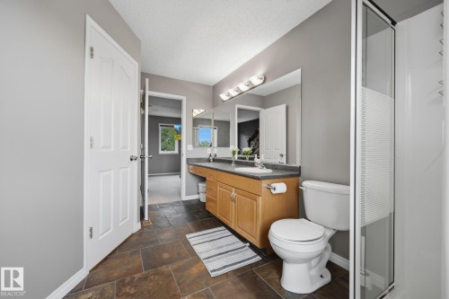 Spacious bathroom featuring a dual vanity with light wood cabinetry, dark countertops, a large mirror, and a glass-enclosed shower - 15 Orchid Place, St. Albert, AB - Indoor Photo Showing Bathroom